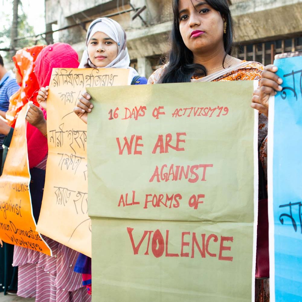 GenderJust_Securing1 A woman holds a poster that reads ‘We Are Against All Forms of Violence’.
