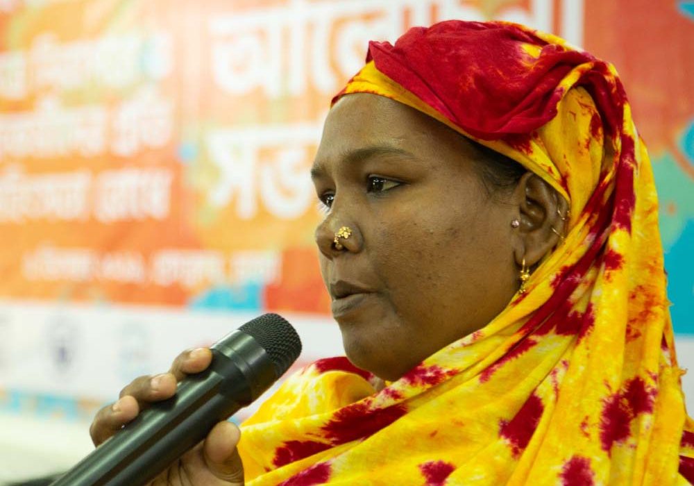GenderJust_Securing2 A woman is holding a microphone and speaking.
