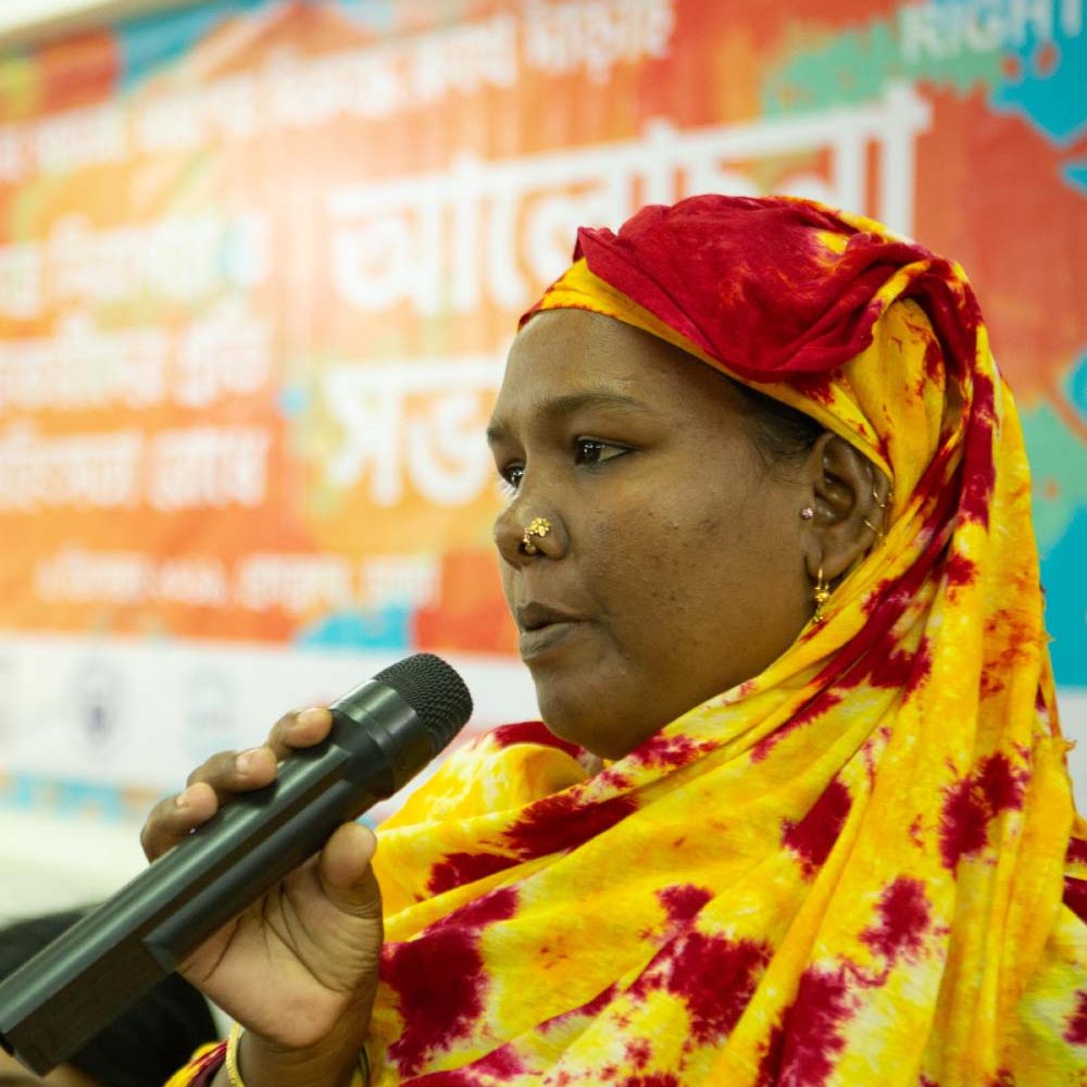 GenderJust_Securing2 A woman is holding a microphone and speaking.