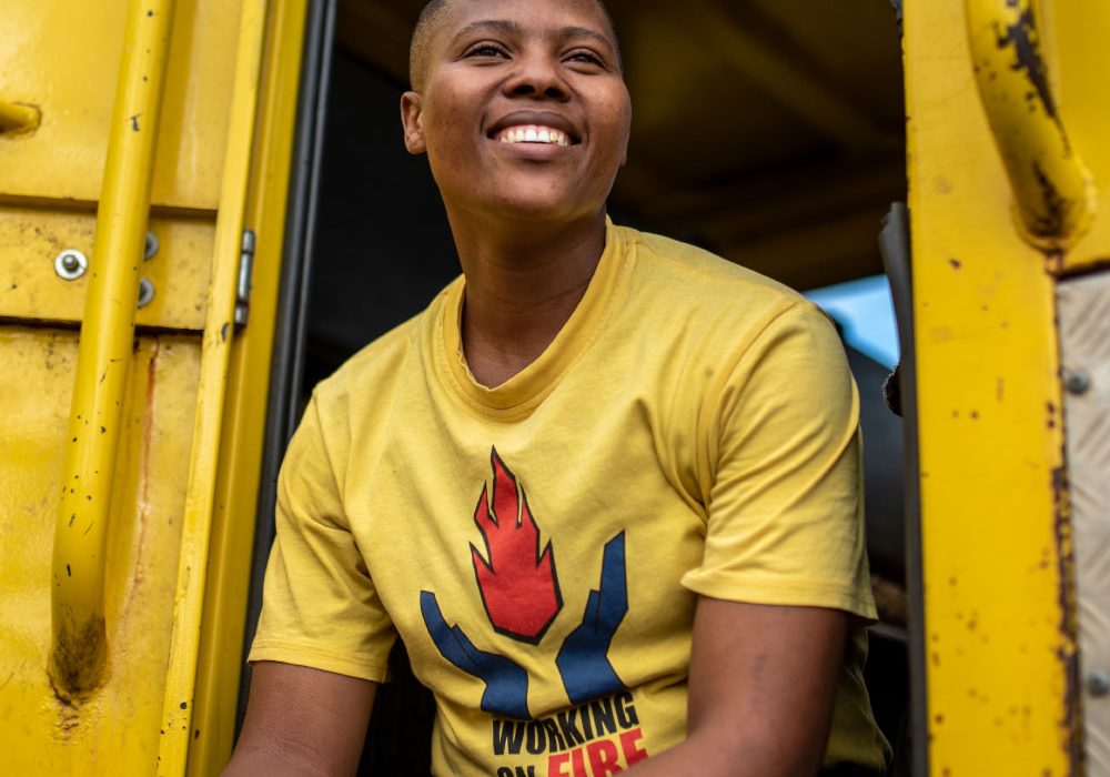Landing_Card_Impact A female firefighter sits in a firetruck, smiling and looking away from the camera.