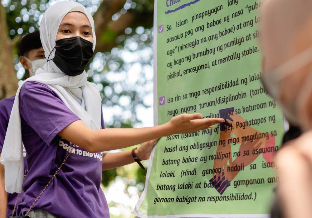 Landing_Slide_CreatingSpaces2 A young woman in the Philippines points to a poster about ending child, early and forced marriage.