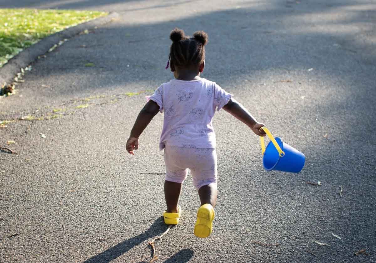 Landing_Slide_InvestCare A toddler holding a toy bucket runs outside.