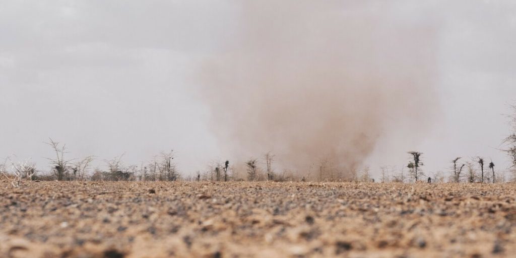 Dust cloud, Wajir Drought A close up of dry, baren, cracked earth with a dust cloud swirling in the background.