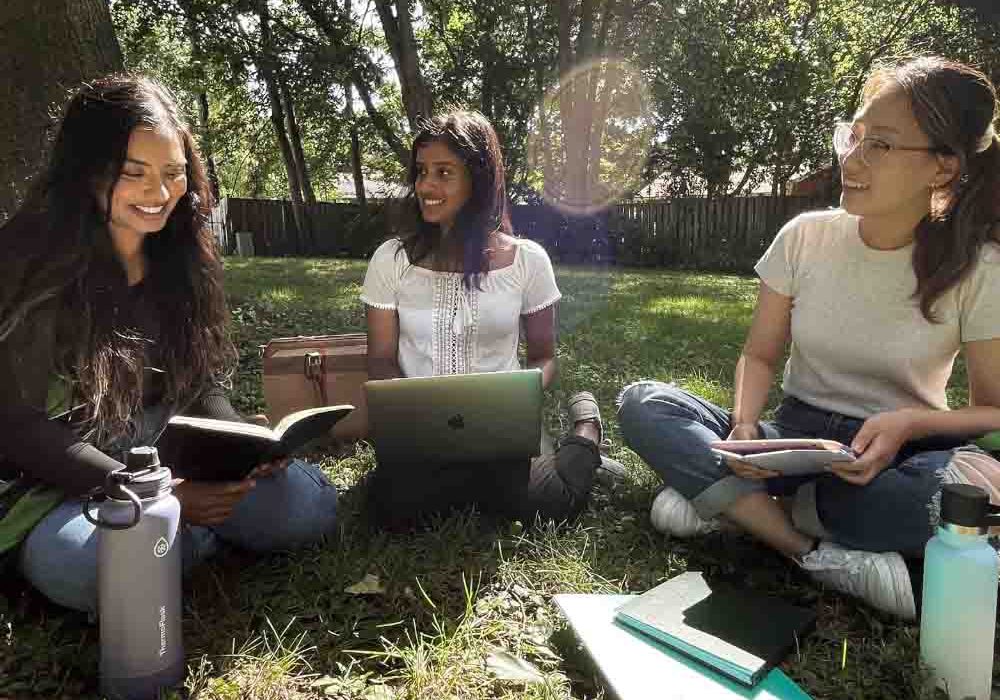 SexualReproductiveRights_HerFuture Three university-aged women are holding a meeting outdoors.
