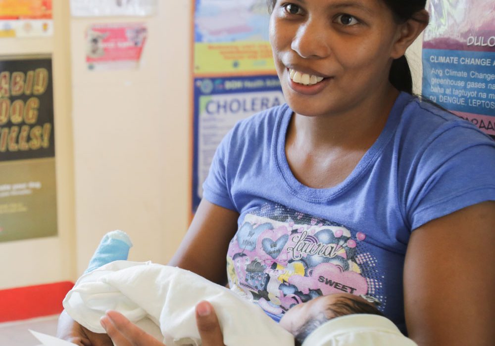SexualReproductiveRights_Hero2 A smiling young mother holds a baby during a medical consultation.